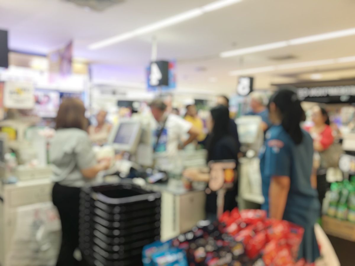 Blurred image of cashier with long line of people at check-out counter of supermarket